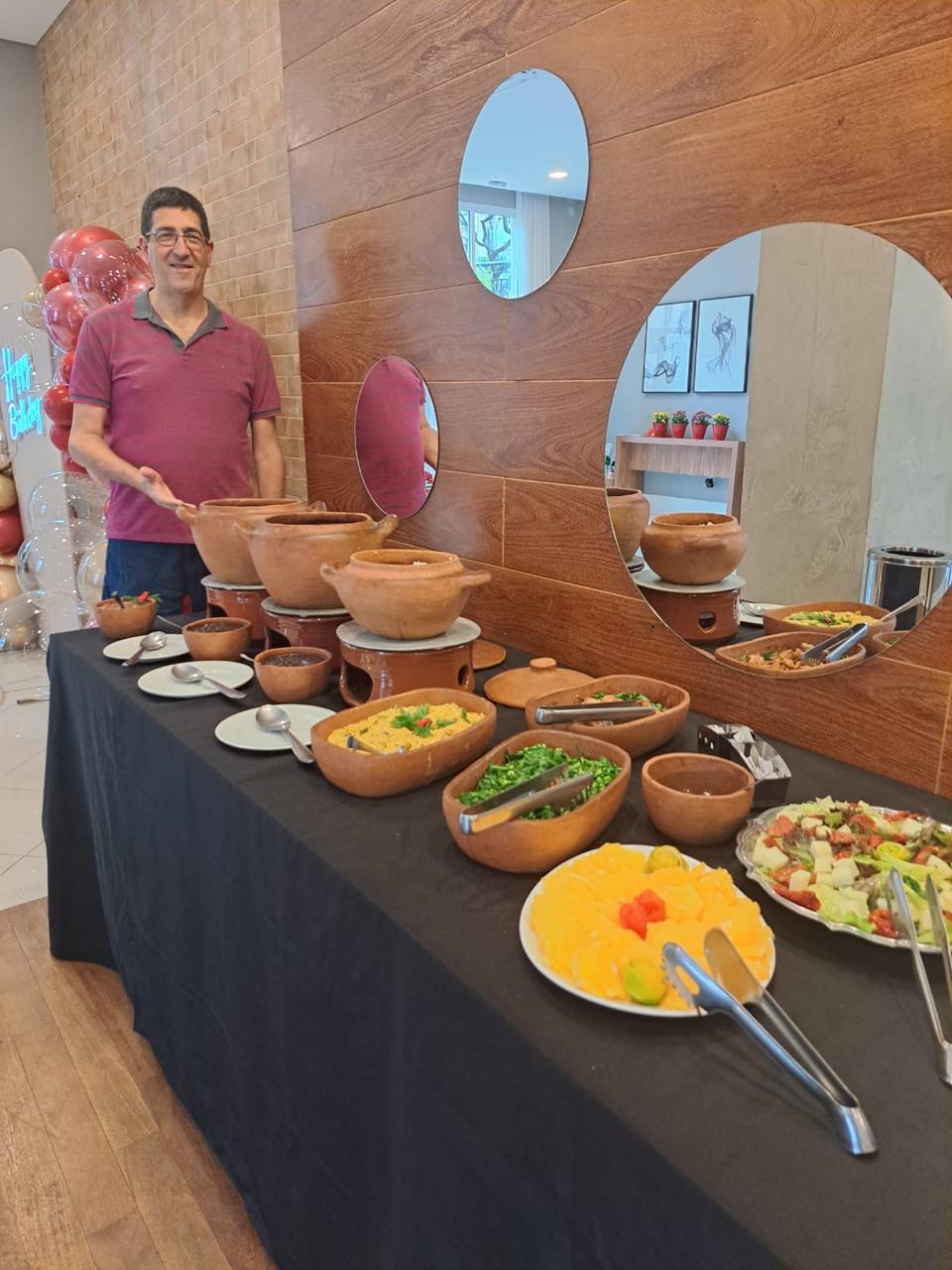 Marcelo Amyuni servindo pratos em potes de barro na mesa de buffet de uma festa