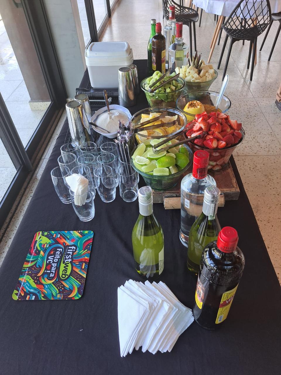 Mesa de bar montada com copos, frutas frescas e bebidas para caipirinhas