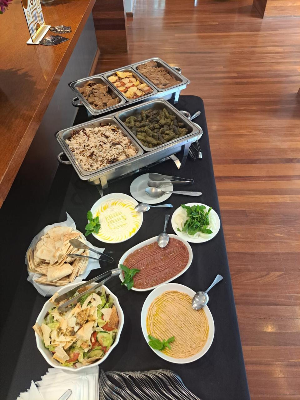 Mesa completa com pastas árabes, fatouch, pão sírio e pratos quentes ao fundo